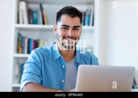 Lachend mexikanischen hipster Mann bei der Arbeit mit Laptop Hallenbad am Schreibtisch zu Hause Stockfoto