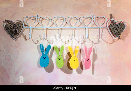 Osterhase auf der Wand im Zimmer begeistert. Mehrfarbige Ostern Kaninchen aus Stoff auf rosa Wand. Hartes Licht vom Fenster und Schatten an der Wand. W Stockfoto