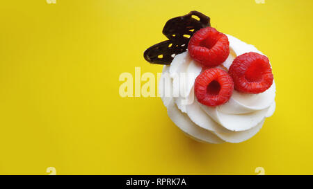 Hausgemachte Muffins mit süßer Sahne und frischen roten Himbeeren auf gelbem Hintergrund. Ansicht von oben Stockfoto