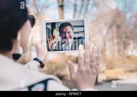 Junge Frau mit einem Tablet-PC durch eine Videokonferenz mit ihren Geschäftsmann Freund, entfernt befindet sich auf einer Geschäftsreise. Konzept des Haltens eines langen DISTAN Stockfoto