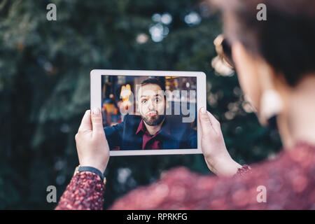 Junge Frau mit einem Tablet, in einer Videokonferenz mit ihrem Geschäftsmann Freund, schickt Sie ist Chat Küsse, während er auf einer Geschäftsreise. Konz Stockfoto