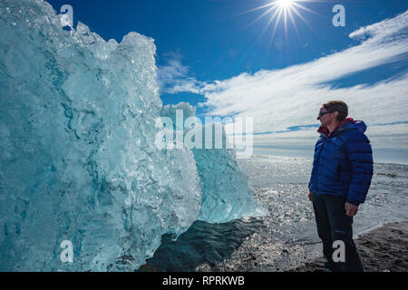 Person, die die Prüfung eines Eisberg auf Breidamerkursandur schwarzer Sandstrand, unter Jokulsarlon ist. Sudhurland, South East Island. Stockfoto