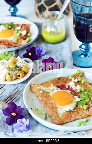 Bretonische traditionelle Pfannkuchen aus Buchweizenmehl mit Schinken, Käse, Ei, Feta, grüne Erbsen und grüne Butter. Frühstück von Buchweizen dünne Pfannkuchen wi Stockfoto