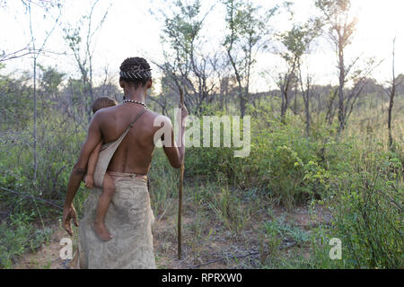 Mutter mit einem Baby der Buschmänner der San Leute Wurzeln für Essen in der Kalahari Wüste, Namibia, Afrika Stockfoto