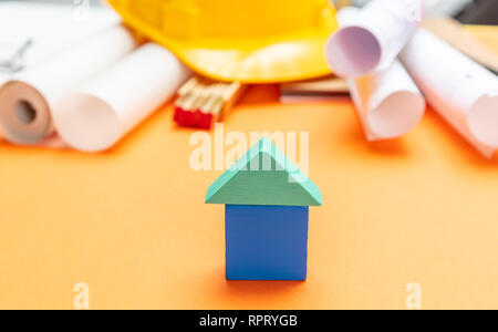 Immobilien Konzept. Kleines haus Modell, Schutzhelm und Projektentwürfe auf orange Farbe Hintergrund Stockfoto