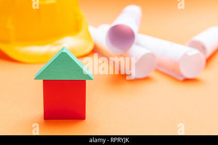 Immobilien Konzept. Kleines haus Modell, Schutzhelm und Projektentwürfe auf orange Farbe Hintergrund Stockfoto