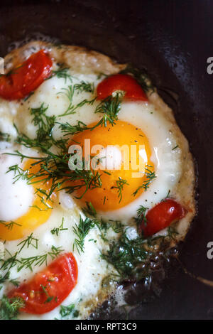 Spiegeleier mit Gemüse und Kräutern, die in der Pfanne, auf dem Feuer auf dem Herd kochen. Ansicht von oben, close-up. Konzept, gesundes Frühstück. Fliegen legen. Stockfoto