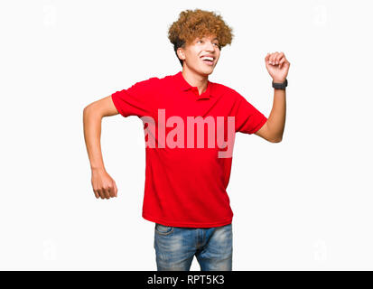 Junger stattlicher Mann mit afro Haar zu tragen rote t-shirt Tanzen glücklich und freundlich, lächelnd, lässig und selbstbewusst Musik hören Stockfoto
