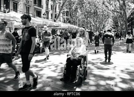 BARCELONA, SPANIEN - Jun 1, 2018: Einheimische und Touristen im Zentrum von Barcelona zu Fuß auf der berühmten Rambla dels Estudis Fußgängerzone mit Frau drücken Senior in Ihrem Rollstuhl Schwarz und Weiß Stockfoto