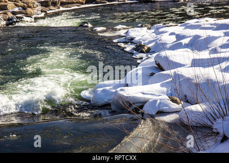 Verschneite Küste neben dem rauschenden Fluss im Winter Stockfoto