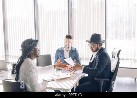 Ernsthafte multi-ethnischen Geschäft Leute am Tisch sitzen, indische Senior Executive Händeschütteln mit seinem Nahen Osten und europäischen Partnern, fo Stockfoto