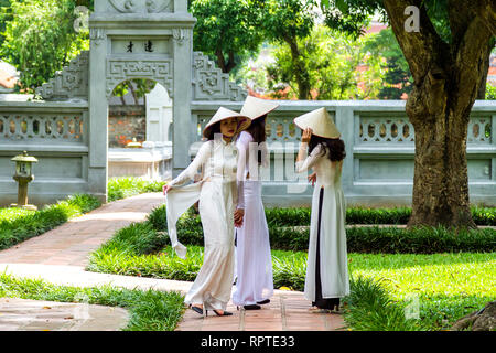 Junge vietnamesische Frauen chatten. Sie tragen die traditionelle Kleidung Ao Dai und der Konischen hat nicht La Lage; Tempel der Literatur in Hanoi, Vi Stockfoto