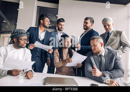 Multirassischen, auf verschiedene Art und Weise gekleidet, Unternehmer sammeln sich um die jungen afrikanischen Weiblicher Kopf Assistant mit Dokumenten, bereit zu unterzeichnen Vertrag Stockfoto