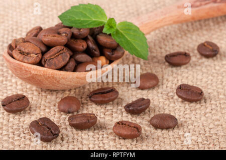 Kaffeebohnen in eine hölzerne Schaufel mit grünen Blättern auf Sack Stockfoto