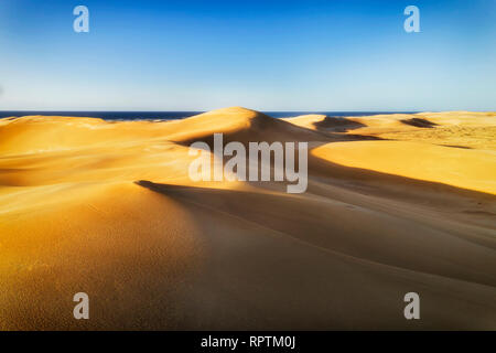 Gelbe Sonne leuchtet Sands in ariden Wüstenklima der Dünen um Stockton Strand an der Pazifikküste von Australien - Ansicht gegen Horizont über Meer unter blauem Sk Stockfoto