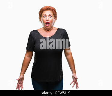 Attraktives senior kaukasischen rothaarige Frau über isolierte Hintergrund Angst und mit Erstaunen Ausdruck, Angst und aufgeregt Gesicht schockiert. Stockfoto