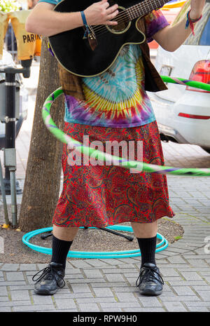 Mann, der Hippie style Kleidung spielen Gitarre und twirling ein Hula Hoop auf Straße Ecke Stockfoto