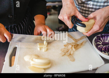 Frau Hände schälen Kartoffeln. Peelings auf Holz Schneidebrett Stockfoto