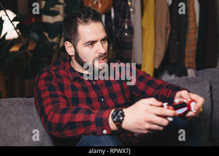 Porträt eines jungen Mannes spielen Videospiele, betonte über das Ergebnis, auf dem Rand seines Sitzes auf der Wohnzimmer Couch. Stockfoto