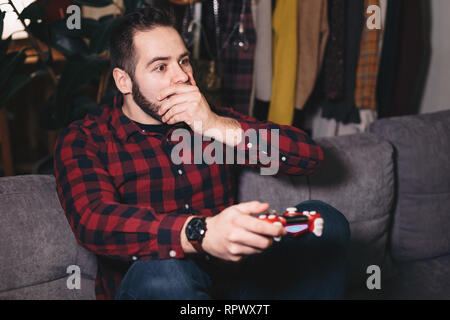 Porträt eines jungen Mannes Spielen von Videospielen, die auf dem Rand seines Sitzes auf der Wohnzimmer Couch. Stockfoto