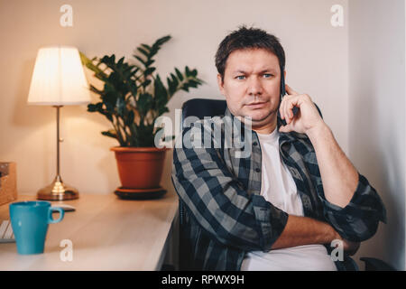 Junge Freiberufler über sein Smartphone gerichtet, auf der Suche nach Geschäftsmöglichkeiten aus Home Office. Stockfoto