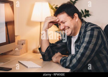 Glückliche junge männliche Freelancer arbeiten vom Home Office, lächelnd und seine Zeit. Stockfoto