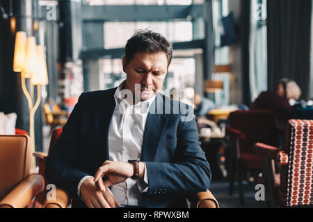 In der Nähe der gut aussehende junge Mann sitzt in einem Café Bar, mit Blick auf seine Hand beobachten, wie er darauf warten, dass jemand kommt und eine geschäftliche Besprechung haben Stockfoto