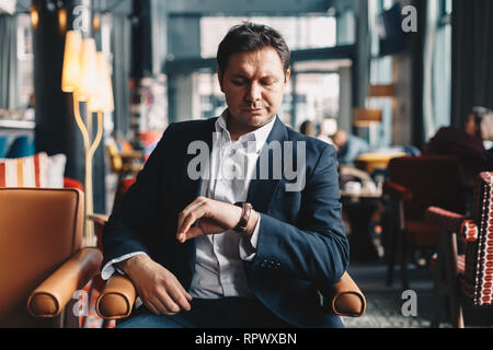 In der Nähe von eleganten jungen Mann sitzt in einem Restaurant in der Mittagspause von der Arbeit, die Zeit auf seine Armbanduhr. Konzept der Zeit ist Geld. Stockfoto
