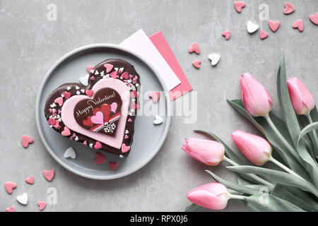 Ansicht von oben am Valentinstag Kuchen in Herzform mit rosa Tulpen und kleinen Herzen mit Grußkarten Stockfoto