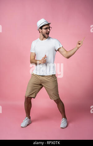 Attraktive lächelnden jungen Mann arm Finger zeigen zu leeren Raum in nur haben signal legere weißes T-Shirt auf rosa Hintergrund isoliert. Stockfoto