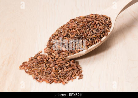 Brauner Reis in einem Löffel aus Holz auf einem Holzbrett. Stockfoto