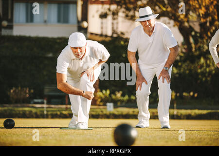 Zwei ältere Männer spielen Boule in einem Park. Ältere Männer genießen Sie eine Partie Boule in einem Rasen auf einem sonnigen Tag. Stockfoto