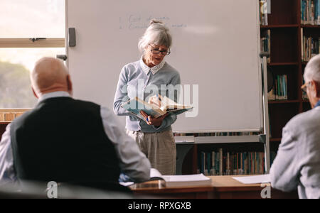 Ansicht der Rückseite zwei ältere Männer, die an einer Universität Unterricht lauschen einem Vortrag. Ältere Frau Professor Unterricht im Klassenzimmer. Stockfoto