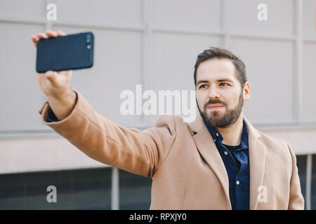 Close-up Portrait von attraktiven und modernen jungen Mann eine selfie mit seinem Handy, das Tragen modischer Kleidung und posieren für Freunde auf Soci Stockfoto