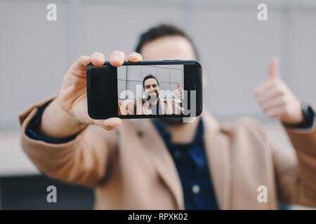 Close-up Portrait von attraktiven und modernen jungen Mann eine selfie mit seinem Handy, das Tragen modischer Kleidung und posieren für Freunde auf Soci Stockfoto