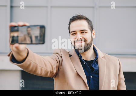 Close-up Portrait von attraktiven und modernen jungen Mann eine selfie mit seinem Handy, das Tragen modischer Kleidung und posieren für Freunde auf Soci Stockfoto