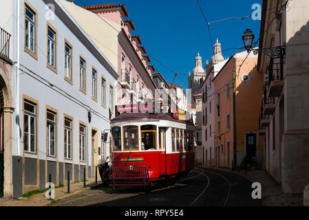 Lissabon, Portugal - 17. Februar 2018: Traditiona Straßenbahn in einer engen Straße in der Alfama Viertel mit der Sao Vicente de Fora Kirche auf dem hinterg Stockfoto