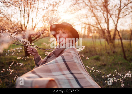 Gerne Frau mittleren Alters entspannen im Frühjahr blühenden Garten bei Sonnenuntergang. Frau gehen und Spaß haben. Muttertag Konzept Stockfoto