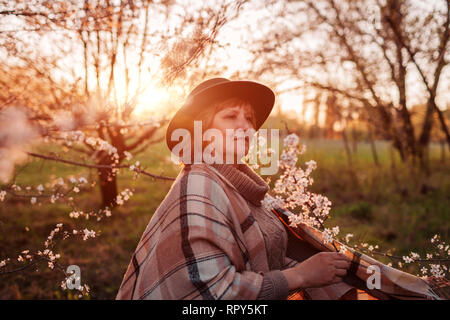 Gerne Frau mittleren Alters entspannen im Frühjahr blühenden Garten bei Sonnenuntergang. Frau gehen und Spaß haben. Muttertag Konzept Stockfoto