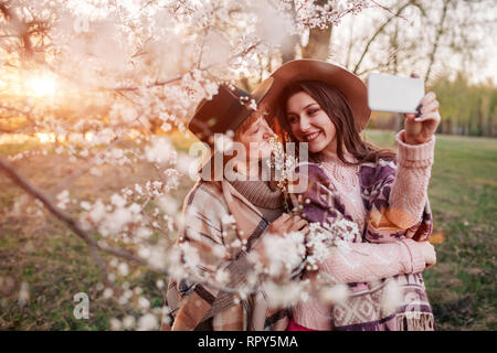 Glücklich im mittleren Alter Mutter und ihrer Tochter umarmen und die selfie in blühende Frühling Garten bei Sonnenuntergang. Muttertag Konzept. Die Werte der Familie Stockfoto