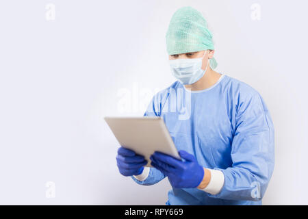 Chirurg Arzt in sterilen Handschuhen Vorbereitung für den Betrieb mit Tablet-PC. Er trägt eine chirurgische Gap und blauem Kleid Stockfoto