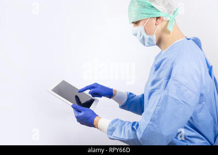 Chirurg Arzt in sterilen Handschuhen Vorbereitung für den Betrieb mit Tablet-PC. Er trägt eine chirurgische Gap und blauem Kleid Stockfoto