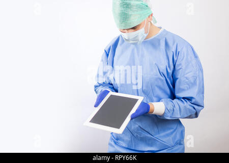 Chirurg Arzt in sterilen Handschuhen Vorbereitung für den Betrieb mit Tablet-PC. Er trägt eine chirurgische Gap und blauem Kleid Stockfoto