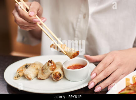 Croped der Frau in weißer Bluse mit Abendessen im Restaurant. Weibliche Hände Maniküre holding Tempura mit Garnelen mit futtersticks. 3-Gänge Mittagessen Stockfoto