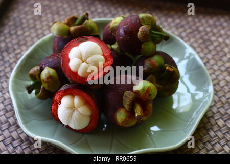 Mangostanfrucht einige offene Hälfte einige ganze Früchte auf dem Grün Keramik Teller. Stockfoto