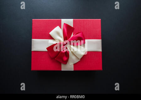 Echten Box mit weißen und roten Bogen und band oben Blick auf Urlaub auf schwarzem Hintergrund isoliert. Flach. Kopieren Sie Platz. Stockfoto