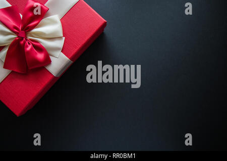 Echten Box mit weißen und roten Bogen und band oben Blick auf Urlaub auf schwarzem Hintergrund isoliert. Flach. Kopieren Sie Platz. Stockfoto