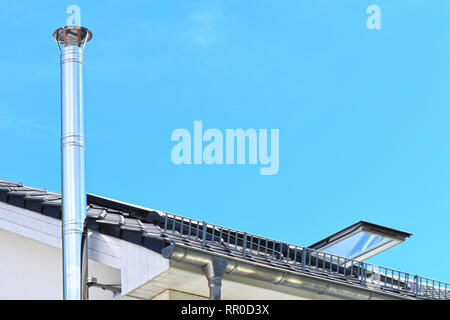 Edelstahl Kamin und Teile des Daches mit einem offenen Dach Fenster vor einem strahlend blauen Himmel. Stockfoto