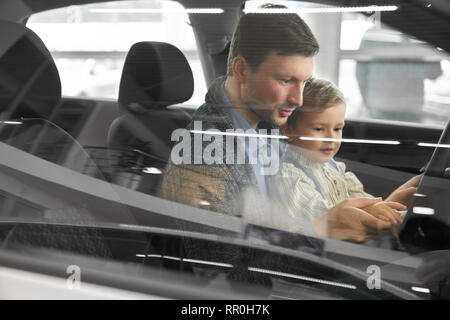 Ansicht von der Seite Fenster, Vater und Sohn im Auto sitzen. Eltern und Kind in der Kabine sitzen, im Fahrersitz am Lenkrad. Potenzielle Käufer die Prüfung der. Stockfoto