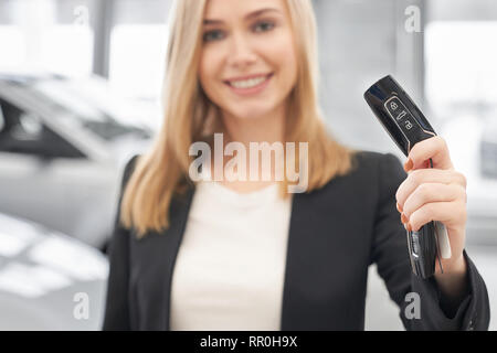 Autoschlüssel close up, schöne Frau mit Schlüssel in der Hand, zeigen, an der Kamera schaut. Professionelle und happy Car Dealer Auto Center lächelnd und im Ausstellungsraum der Händlerniederlassung posieren. Stockfoto